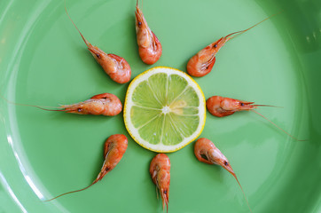 boiled shrimps with a slice of lemon are on a green plate