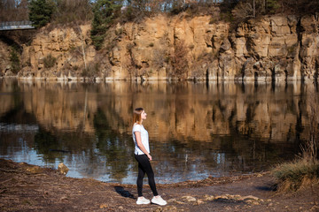 Fototapeta premium Girl walking along the lake shore. A woman in a white shirt enjoyong beautiful view and nice weather