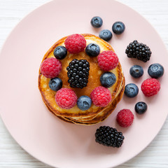 Homemade pancakes with berries on a pink plate over white wooden background, top view. Flat lay, overhead, from above.