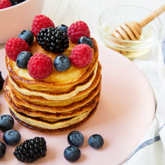 Homemade pancakes with berries and honey on a pink plate, side view. Close-up.