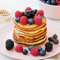 Homemade pancakes with berries and honey on a pink plate, side view. Close up.