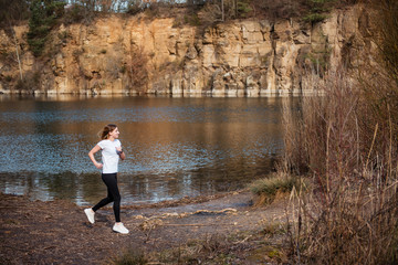 Fototapeta na wymiar Young sporty woman in sportswear running on the lake shore in countryside on summer day.