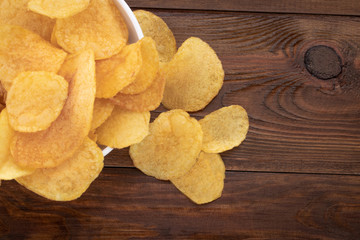 Crispy potato chips in bowl on wooden background, top view