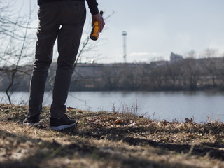 Lonely man with a bottle of beer on the river Bank in cold early spring