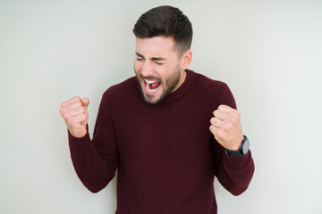 Fototapeta premium Young handsome man wearing a sweater over isolated background very happy and excited doing winner gesture with arms raised, smiling and screaming for success. Celebration concept.