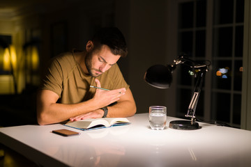 Young handsome man studying at home, reading a book at night