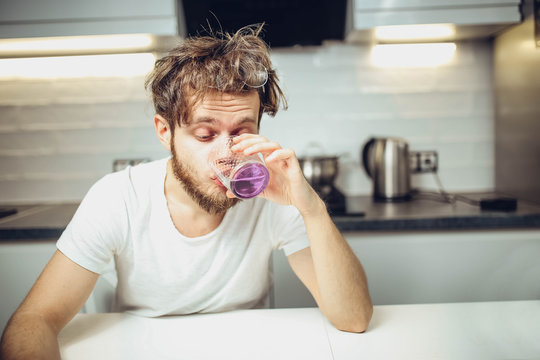 young shaggy man drinks alcohol in the kitchen with a funny face. husband relaxes
