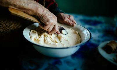 Fototapeta na wymiar hands of an old woman with a wooden spoon, whip homemade butter with whey
