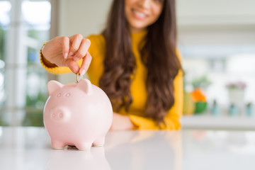 Close up of woman smiling putting a coin inside piggy bank as investment
