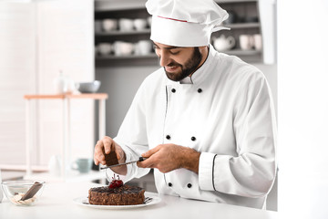 Male confectioner decorating tasty chocolate cake in kitchen