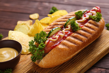 Board with tasty hot dog on wooden background, closeup