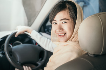 asian muslim with head scarf looking camera while driving car