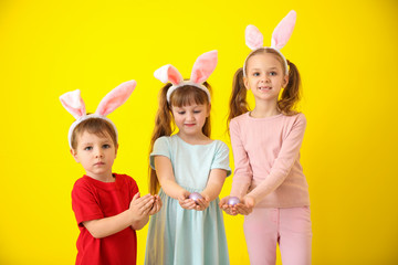 Cute little children with Easter eggs and bunny ears on color background