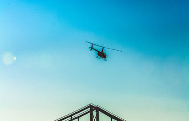 Silhouette of helicopter in blue clear sky with solar patches of light. Warm spring day. Modern transport.