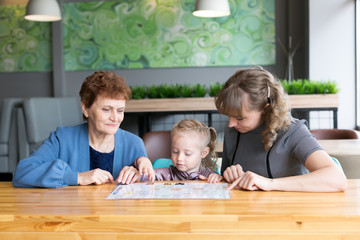 Grandmother's daughter and granddaughter watching the menu in a cafe.