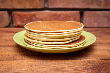 Stack of pancakes on the wooden background on the green dish