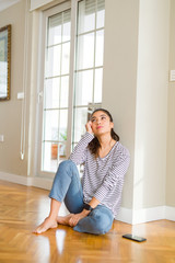 Young beautiful woman thinking and wondering with a hand on chin sitting on the floor at home