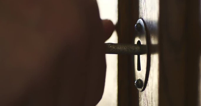 Side wiev of person by hand turns old key in the keyhole of antique wooden cabinet