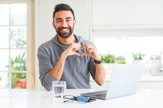 Handsome Hispanic Man Working Using Computer Laptop Smiling In Love Showing Heart Symbol And Shape With Hands. Romantic Concept.