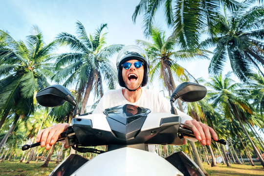 Man in safe helmet riding a motorbike under palm trees wide angle shoot