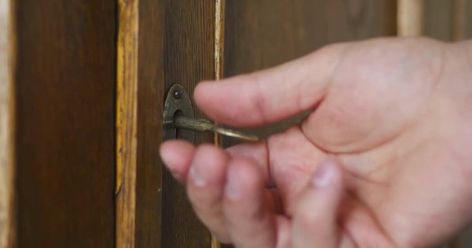 Side wiev of person by hand turns old key in the keyhole of antique wooden cabinet