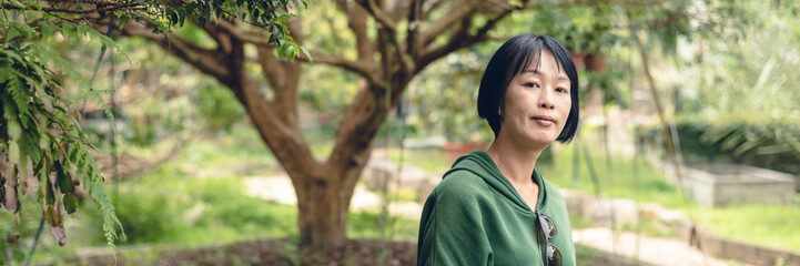 portrait of Asian mature woman stand at the fruit farm, banner of travel and technology concept