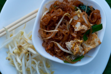 Fried noodle Thai style with egg on with White dish with chopsticks and banana leaf floor.