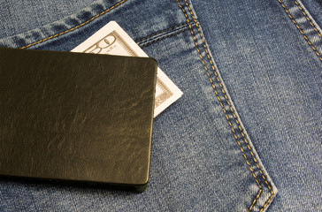 Black leather wallet with money in back blue jeans pocket denim background texture.