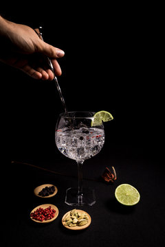 barman preparing a gin and tonic cocktail on a black background next to his ingredients