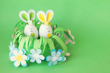 Easter holiday concept with cute handmade funny eggs bunny  in a homemade paper flower basket with a greeting text