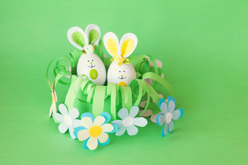 Easter holiday concept with cute handmade funny eggs bunny  in a homemade paper flower basket with a greeting text