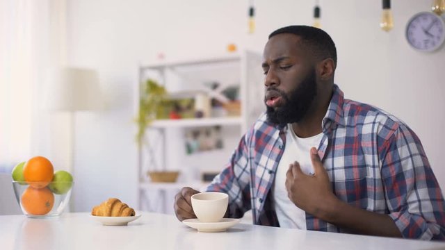 African-American male drinking coffee, coughing after chocking with beverage