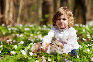 Little girl  play with real rabbit in the garden. Cute child at Easter egg hunt with  pet bunny. Spring outdoor fun for kids with pets