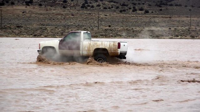 Filthy white pieced together truck mud bogging playing in a deep puddle