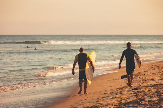 Two surfers walking down the beach with their surfboards - Powered by Adobe