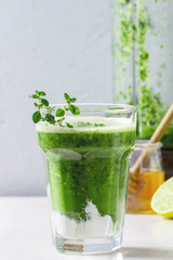 Green spinach kale apple honey smoothie with yogurt and thyme in glass on white marble table with blender and ingredients above. Healthy organic eating.