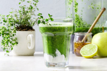 Green spinach kale apple honey smoothie with yogurt and thyme in glass on white marble table with blender and ingredients above. Healthy organic eating. Close up