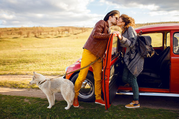 Beautiful portrait of young couple, near vintage red car, with their husky dog, isolated on a nature background.