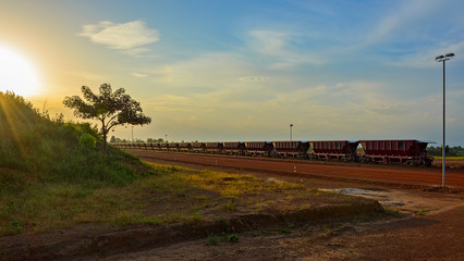 Sunset view to railway carriages for transportation of bauxite ore on train tracks at the end of the railway line from bauxite mining. Guinea, Africa.