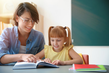 Fototapeta premium Teacher with pupil reading book at table in classroom, space for text