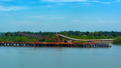 Outdoor incline large covered conveyor with rubber belt for transportation from an storage outside area to transhipment into a capesize bulk carrier ships in the Kamsar, Guinea, Africa.