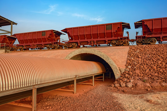 A freight train carrying bauxite in railway carriages for transhipment into a capesize bulk carrier ships by covered conveyor belt mechanism in the Kamsar, Guinea, Africa.
