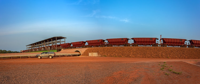 A freight train carrying bauxite in railway carriages for transhipment into a capesize bulk carrier ships by covered conveyor belt mechanism in the Kamsar, Guinea, Africa.