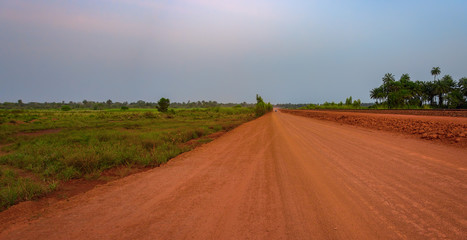 Sunset view of a typical red soils unpaved rough countryside road in Guinea, West Africa.