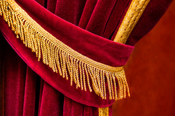Close up detail of open and ruffeld red curtain with golden fringes tassel with blurred background...