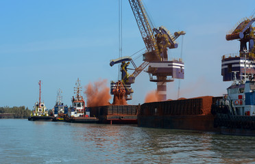 Loading bauxite ore on cargo ship with crane and bucket. Shipment from an storage outside area to a...