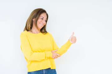 Beautiful middle age woman wearing yellow sweater over isolated background Looking proud, smiling doing thumbs up gesture to the side