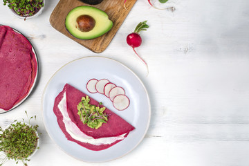 Tasty appetizing beetroot pancakes served on plate with avocado, sprouts and pink radish, white...