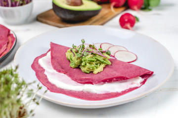 Tasty appetizing beetroot pancakes served on plate with avocado, sprouts and pink radish, white wooden table