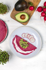 Tasty appetizing beetroot pancakes served on plate with avocado, sprouts and pink radish, white wooden table